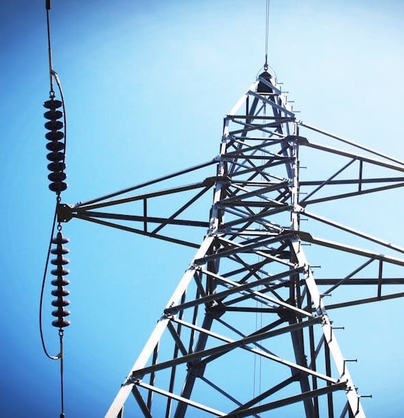 Low angle view of an industrial power transmission tower against a clear blue sky.