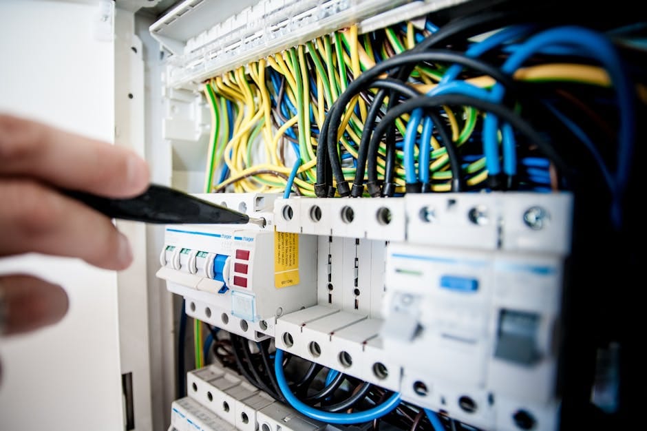 Услуги Hand of electrician working on a circuit breaker panel with colorful wires, ensuring safe electrical connections.