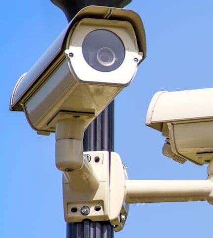 Outdoor security cameras mounted on a pole against a clear blue sky, ensuring vigilant surveillance.